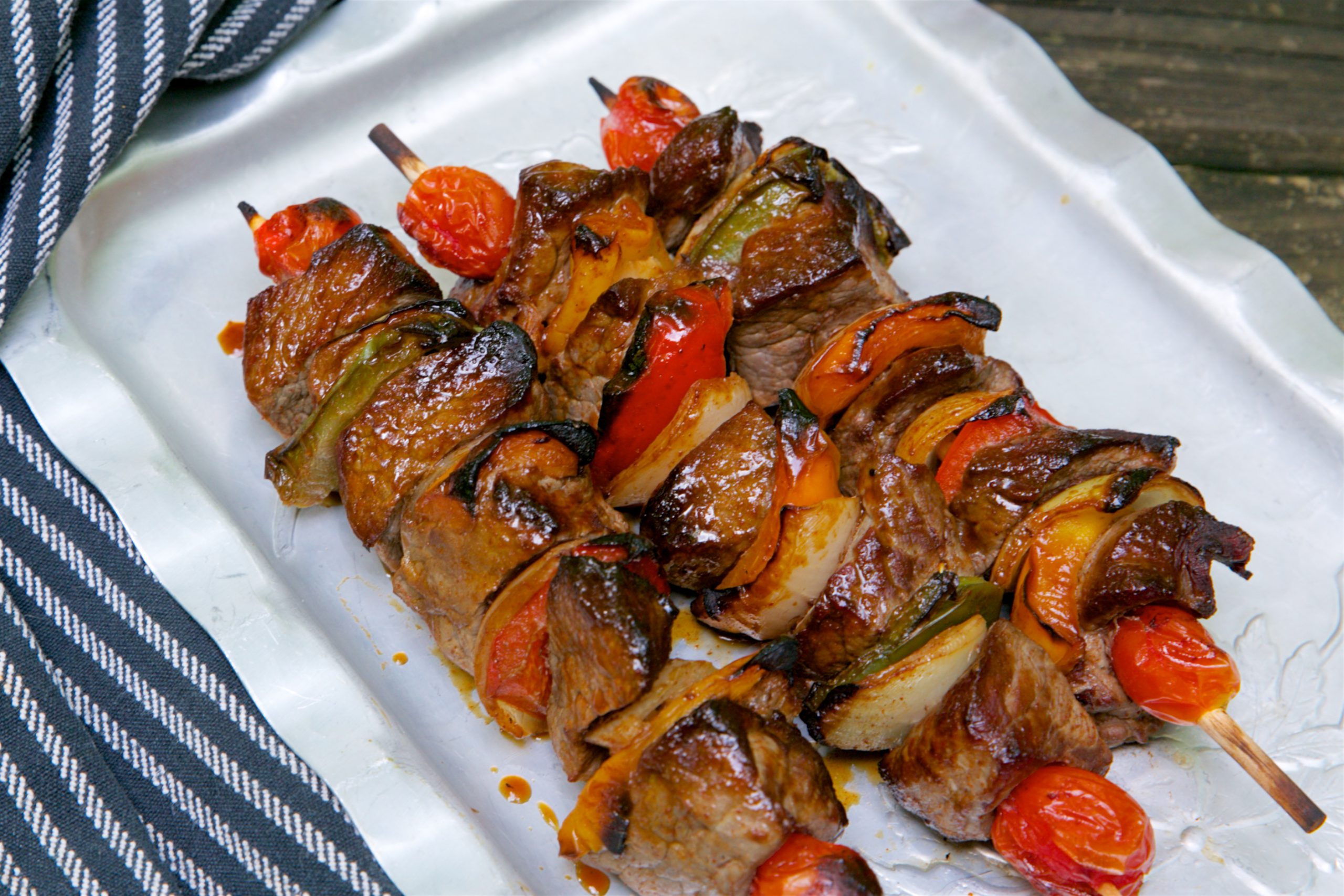 Spicy Szechuan Beef Kabobs on a plate drizzled with San-J Soy Sauce